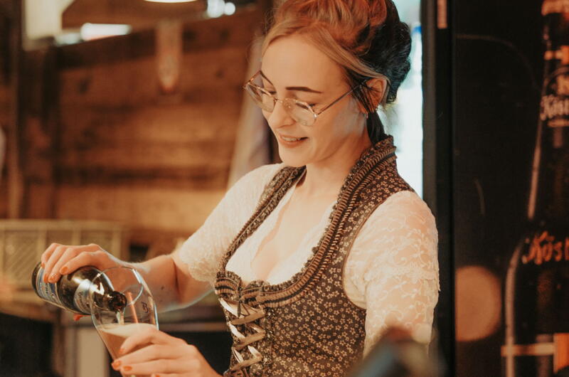 Junge Frau im Dirndl füllt Bier in ein Glas in der Heimatalm