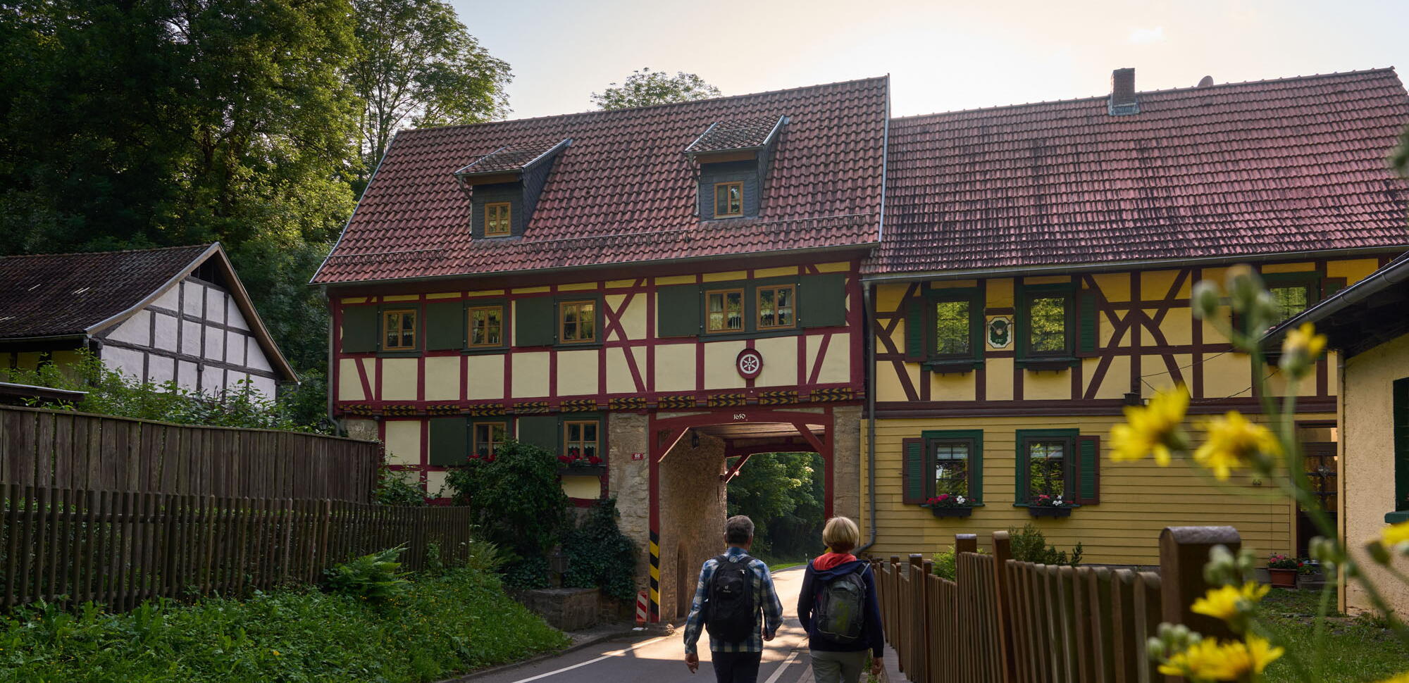 Wanderer am Grenzhaus Heyerode, durch dessen enges Tor eine schmale Straße führt