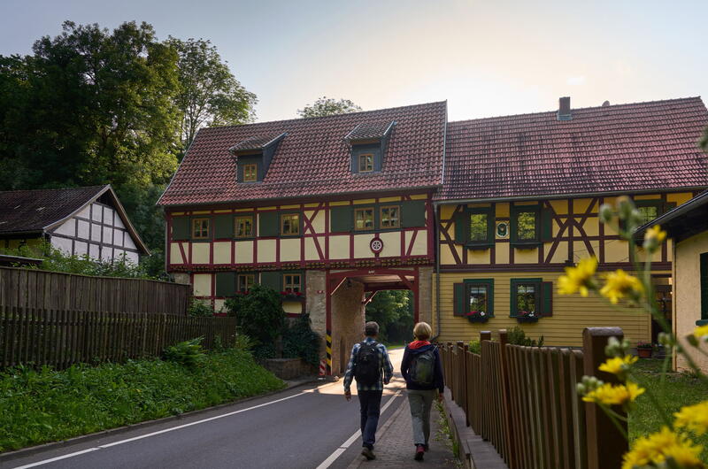 Wanderer am Grenzhaus Heyerode, durch dessen enges Tor eine schmale Straße führt