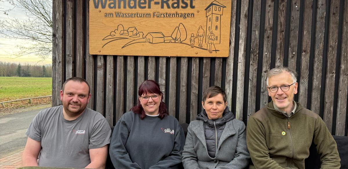 Vier Personen sitzen an einem Holztisch unter dem Schild "Wander-Rast"