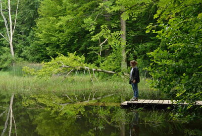 Eine junge Frau steht am Hünenteich, einem wassergefüllten Erdfall und einem der wenigen stehenden Gewässer im Nationalpark Hainich, auf einem Steg.