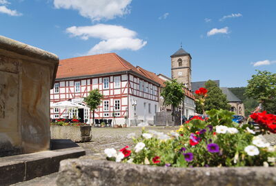 Markt in Creuzburg mit Brunnen und Blumendetail im Vordergrund. Im Hintergrund sind Kirche und Fachwerkhäuser zu sehen.