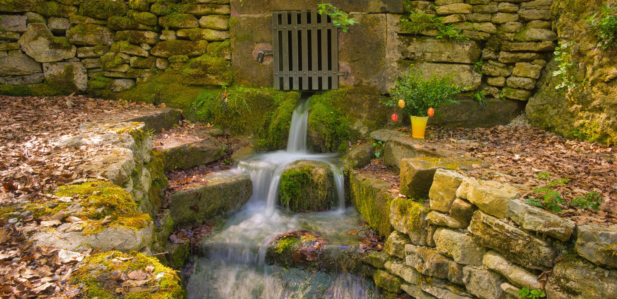 Kleiner Born in Fürstenhagen - Wasser fließt über Steinstufen umrahmt von Natursteinmauern