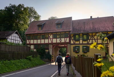Wanderer am Grenzhaus Heyerode, durch dessen enges Tor eine schmale Straße führt