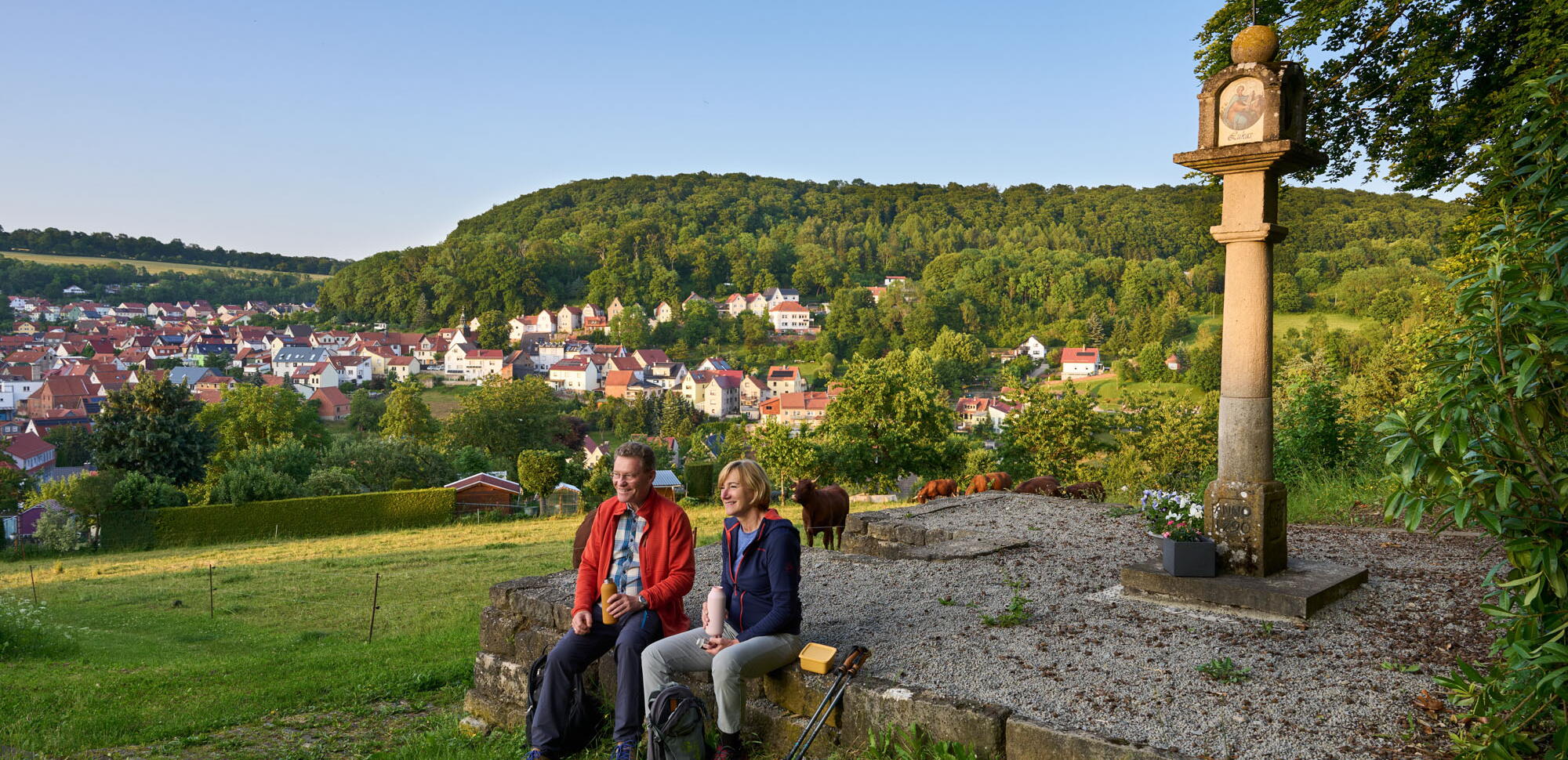 zwei Wanderer machen Pause am Bildstock oberhalb von Heyerode im Eichsfeld