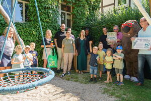 Eine Gruppe Erwachsener und Kinder steht am Rand eines Spielplatzes vor dem neuen Hochbeet.