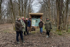 Eine Gruppe von sieben Personen steht im winterlichen Wald um eine Infotafel.