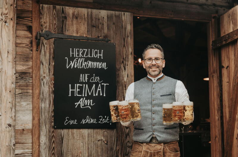 Heimatalm-Betreiber Christian Mehler mit Biergläsern am Eingang