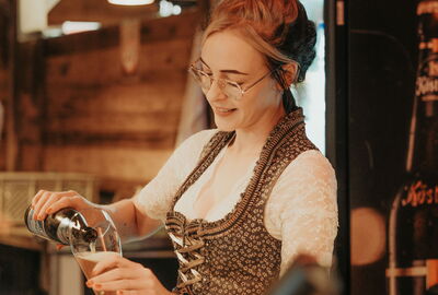 Junge Frau im Dirndl füllt Bier in ein Glas in der Heimatalm