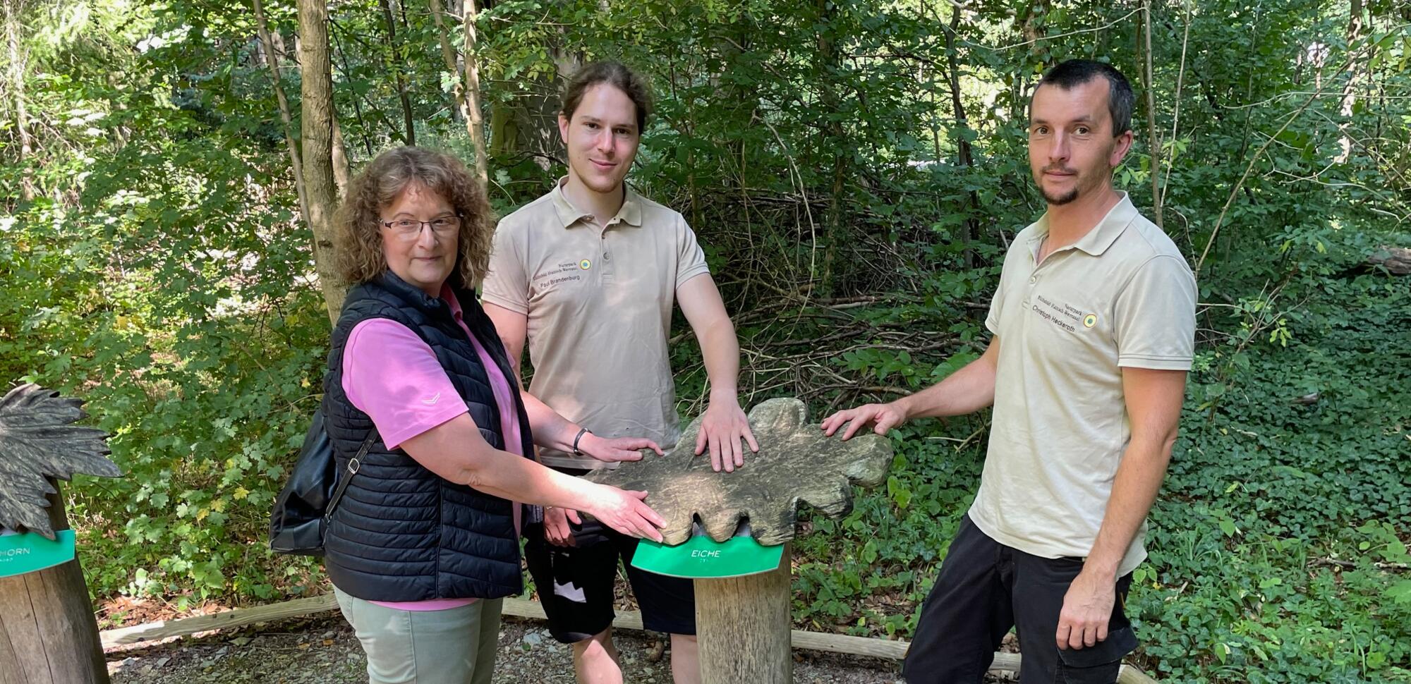 v.l.n.r. Silke Senge vom Blinden- und Sehbehindertenverband Thüringen e.V., Kreisorganisation Eichsfeld, sowie die Naturpark-Ranger Paul Brandenburg und Christoph Heckeroth an einer Taststation auf dem Erlebnispfad im Naturparkzentrum Fürstenhagen.
