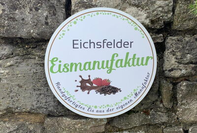 zu sehen ist das Logo, rund und weiß mit hellgrüner Schrift vor einer Wand