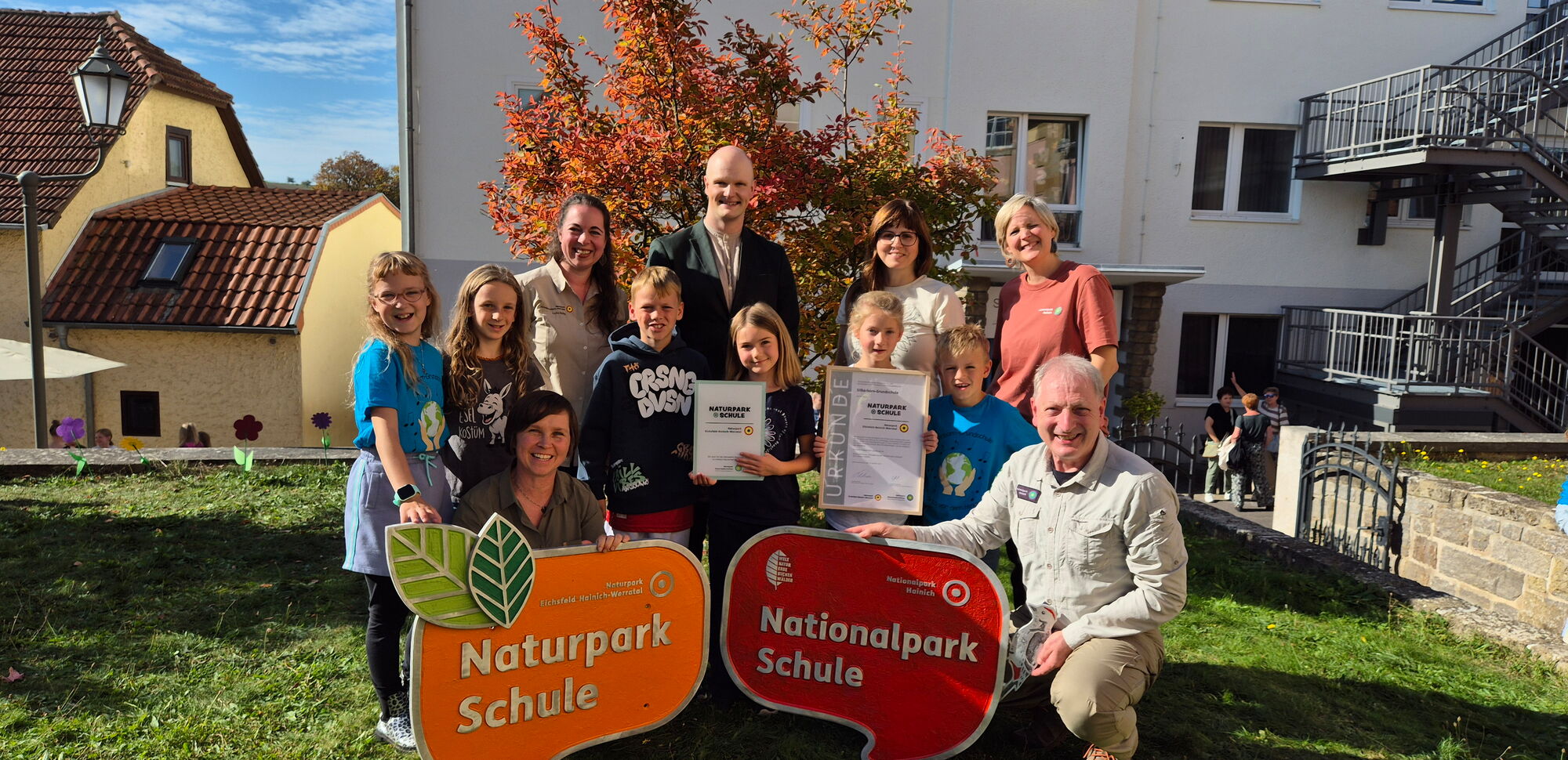 Verantwortliche vom Naturpark und der Schule präsentieren gemeinsam mit Schülerinnen und Schülern die großen Auszeichnungsschilder als Naturpark-Schule und Nationalpark-Schule.