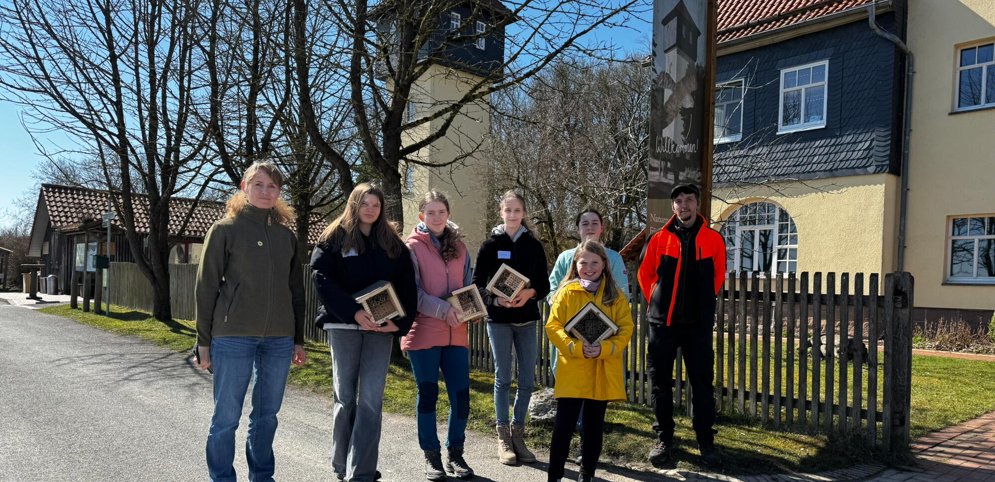 Sieben Personen stehen auf einer Straße vor der gelben Fassade des Naturparkzentrums, einige halten Wildbienen-Nisthilfen in den Händen.
