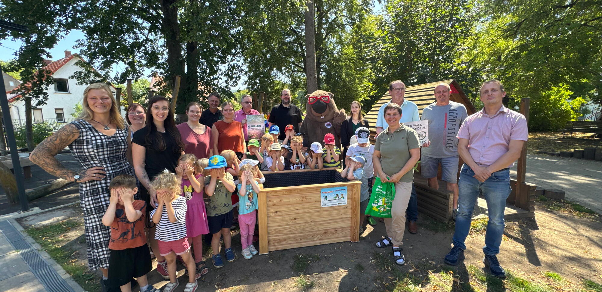 Eine Gruppe Erwachsener und Kinder stehen um ein neues Hochbeet.