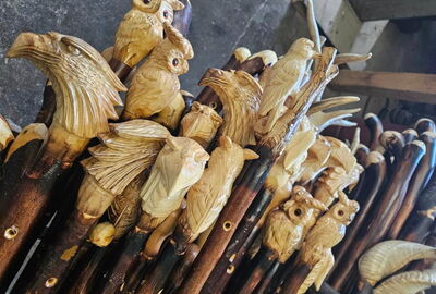 Mehrere handgeschnitzte Wanderst?cke aus Holz mit kunstvoll gestalteten Tiermotiven als Griffst?cke, darunter Eulen und Greifv?gel. Die detailreich bearbeiteten Stockk?pfe stehen dicht nebeneinander in einer Werkstatt und zeigen traditionelle Handwerkskun