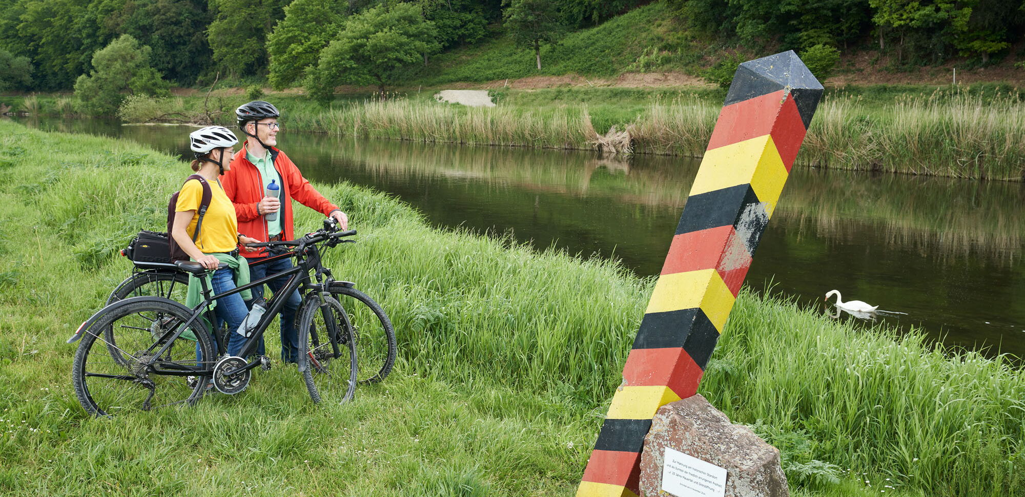 Zwei Radfahrer am Werratalradweg in Lindewerra mit Grenzstele der ehemeligen innerdeutschen Grenze am grünen Band