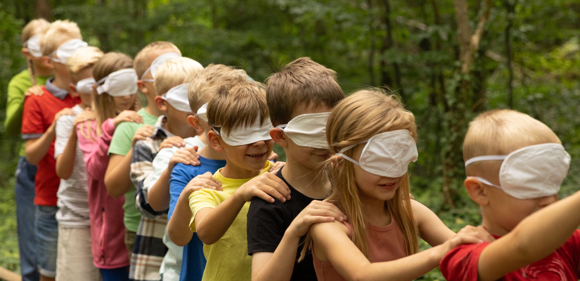 Kinder bilden eine Reihe und haben Augenbinden auf, so laufen sie durch den Wald