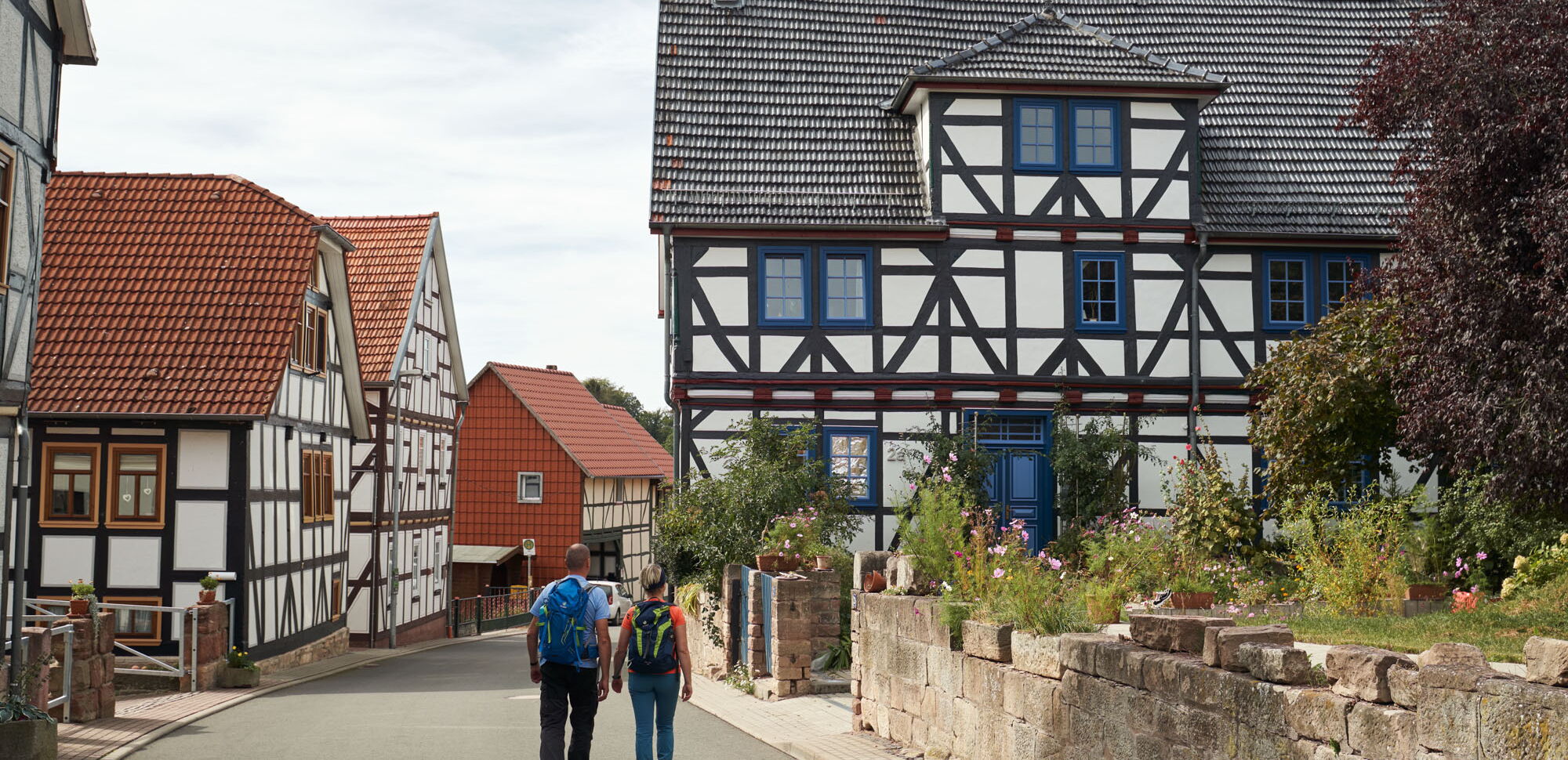 Zwei Wanderer auf dem P16 in Asbach-Sickenberg mit idyllischen Fachwerkhäusern und Höfen.
