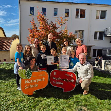Verantwortliche vom Naturpark und der Schule präsentieren gemeinsam mit Schülerinnen und Schülern die großen Auszeichnungsschilder als Naturpark-Schule und Nationalpark-Schule.